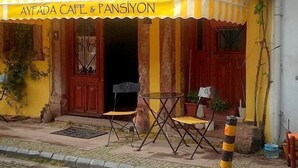 Un café avec un auvent rayé jaune et blanc, des tables en terrasse et une façade rustique.