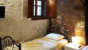 Une chambre rustique comprenant un lit, une table de chevet, une armoire en bois et une fenêtre dont les volets sont ouverts.