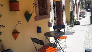 Un café en plein air doté d’un auvent rayé jaune et blanc, avec des tables et des chaises disposées à l’extérieur, et des jardinières suspendues au mur.