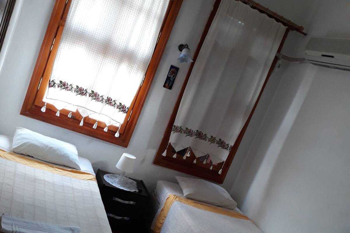 Une chambre avec deux lits simples, une petite table avec une lampe et une fenêtre avec des rideaux.