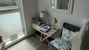 Ett rum med ett stort fönster, ett skrivbord med en lampa, en stol och en spegel på väggen.