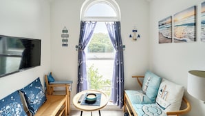 Una habitación con televisor, sofá, sillón, una mesita y una ventana con cortinas.