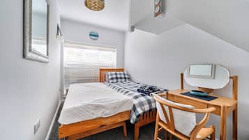 A bedroom with a bed, a desk, a chair, a mirror, and a wall clock.
