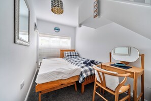 Une chambre à coucher comprenant un lit, un bureau, une chaise, un miroir et une horloge murale.