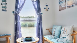 Una habitación con vistas a un cuerpo de agua, un sofá con cojines de temática náutica, una mesita con un cuenco y una pared decorada con motivos marineros.