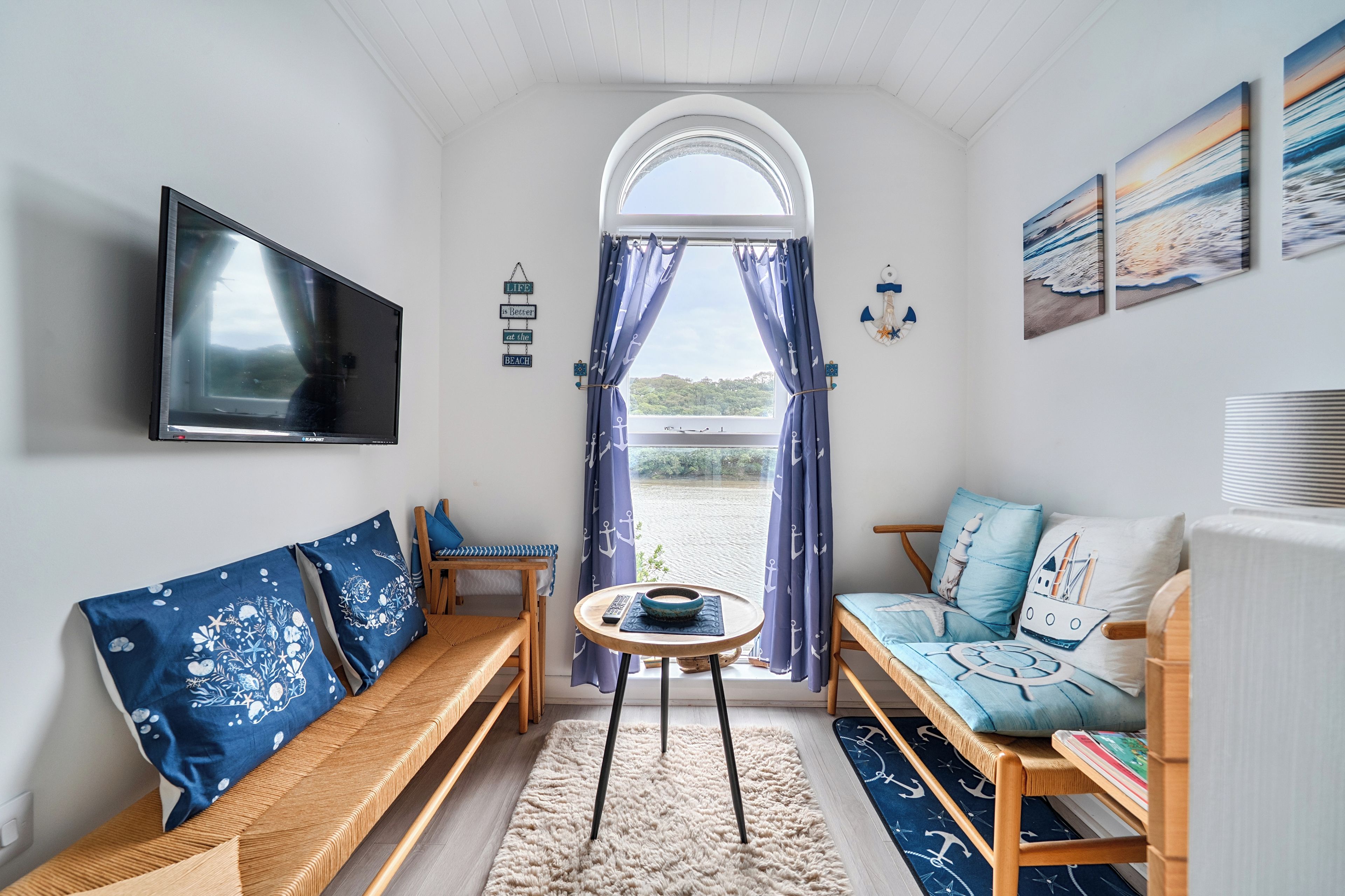 Una habitación acogedora con televisor, sofá, banco y vistas a la playa.