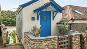 Un pequeño edificio de un piso con una puerta azul y un letrero que indica que es 'The Beach Hut Malpas'.
