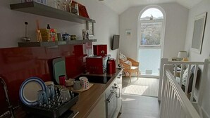 Ett smalt kök med vita skåp, en träbänkskiva och en röd vattenkokare. Det finns röda hänglampor och ett fönster med utsikt över ett snötäckt landskap.