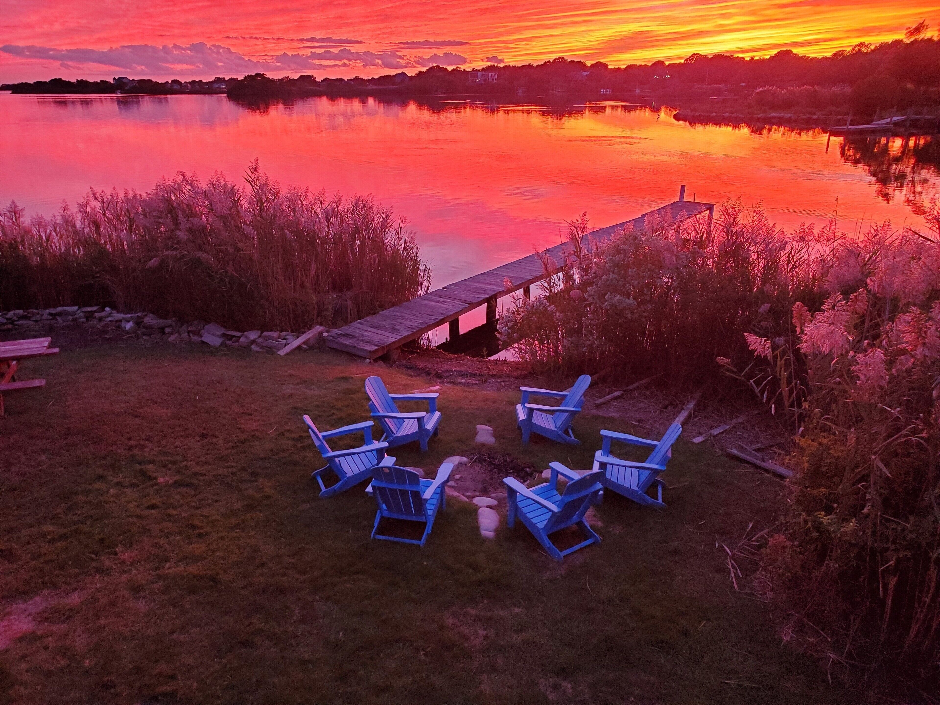 Une vue sur le lac, avec une jetée en bois et des chaises Adirondack bleues disposées pour créer un espace de détente.