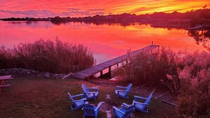 A lakeside view with a wooden dock and blue Adirondack chairs arranged for seating.