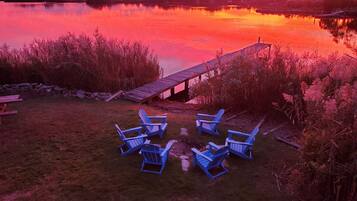 Une vue sur le lac, avec une jetée en bois et des chaises Adirondack bleues disposées pour créer un espace de détente.