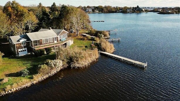 A lakeside property with a house, dock, and surrounding vegetation.