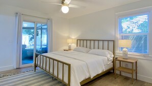 A bedroom with a bed, a nightstand, a ceiling fan, a window with blinds, and a view of the outdoors.