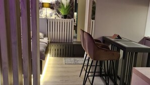 Ett modernt vardagsrum med en soffa, ett matbord och stolar. Det finns en krukväxt på väggen och en lampa på bordet.