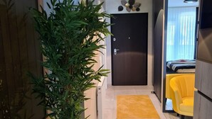 Een moderne hotelgang met een potplant, een gele stoel en een bed met een gestreept dekbed.
