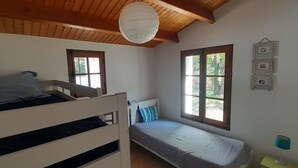 A room with a bunk bed, a single bed, a window with a view of greenery, a hanging light fixture, and a wall-mounted picture frame. - Beautiful Vendée house 50 meters from the beach, sleeps 2 to 10, depending on the season. (La Guérinière)