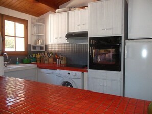 Una cuina compacta amb armaris blancs, taulell amb rajoles vermelles, rentadora i forn negre.