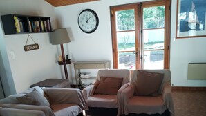 A cozy living room with two sofas, a coffee table, a clock, and a window with a view of trees. - Beautiful Vendée house 50 meters from the beach, sleeps 2 to 10, depending on the season. (La Guérinière)