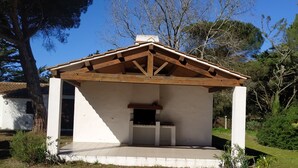 A small, white, single-story building with a wooden roof and a built-in grill area. - Beautiful Vendée house 50 meters from the beach, sleeps 2 to 10, depending on the season. (La Guérinière)