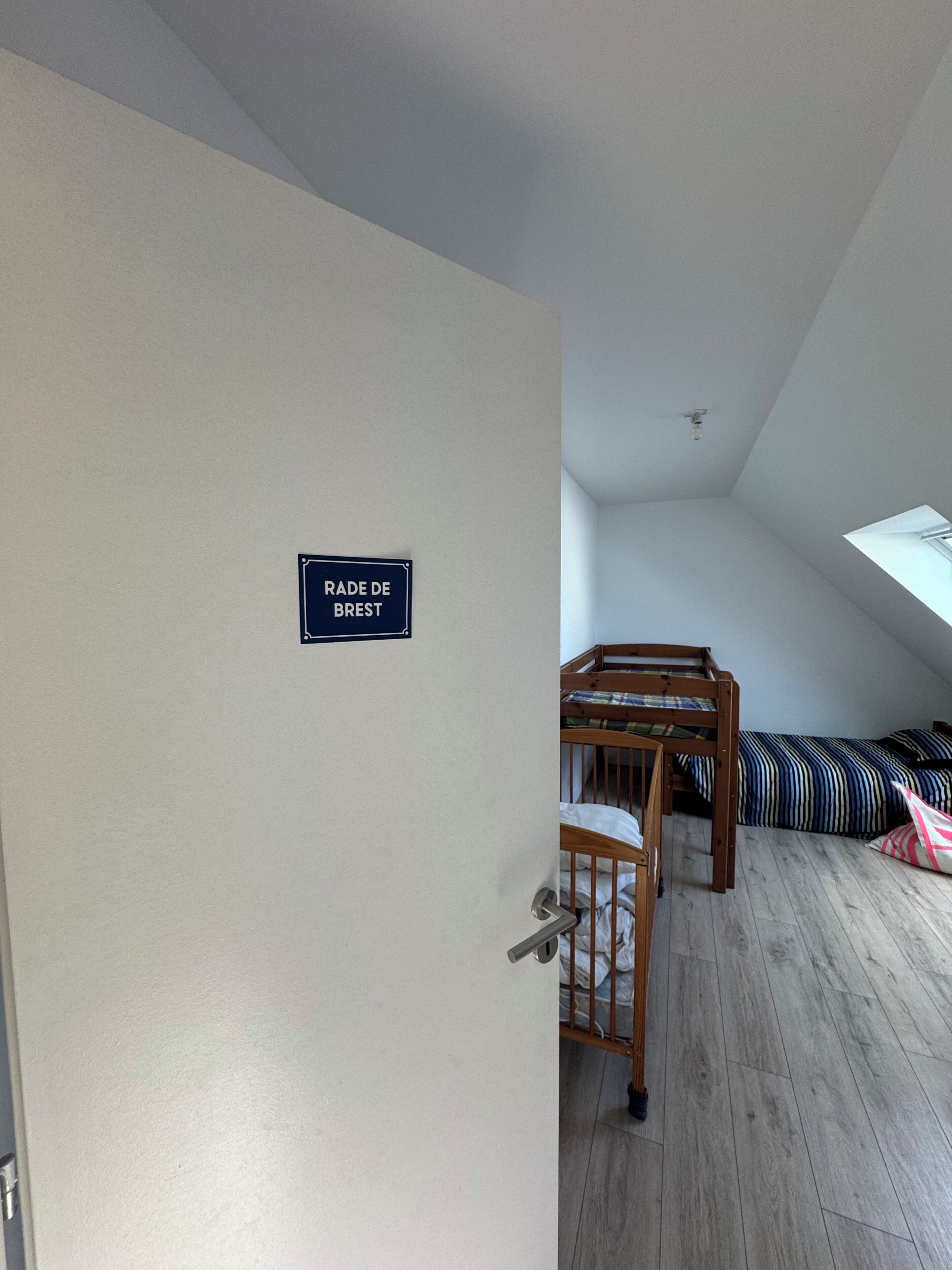 Una habitación con literas, una puerta con un cartel que dice 'RADE DE BREST' y un tragaluz.