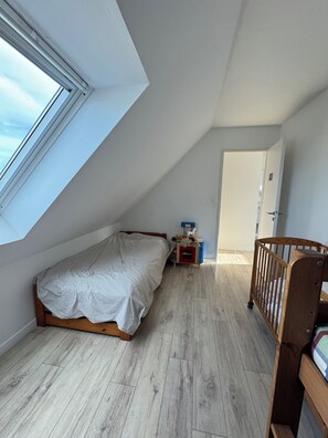A room with a sloped ceiling, a bed, a crib, a small table, and a door. - MEZOU BRAS (LANDUNVEZ)