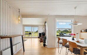A spacious kitchen with wooden flooring, a dining area with a table and chairs, and a view of the outdoors through large windows. - Gorgeous home in Millinge with sauna (Millinge)