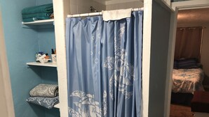 Ein Badezimmer mit blauer Duschvorhang, weißem Ablagefach mit Handtüchern und Toilettenpapierhalter.