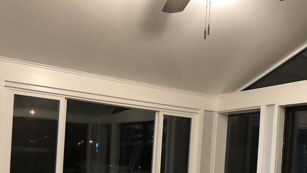 Ein Zimmer mit großen Fenstern, einem Deckenventilator und einer Holzwand mit Dekorationen.