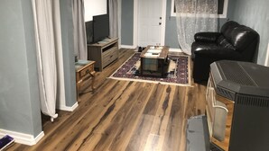 Ein Wohnzimmer mit Holzboden, einer schwarzen Ledersofa, einem Fernseher, einem kleinen Tisch und einem Kamin.