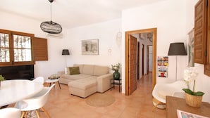 Ein Wohnzimmer mit einem beigen Sofa, einem Esstisch mit Stühlen, einem kleinen Beistelltisch mit einer Vase und einem Flur, der in einen anderen Raum führt.