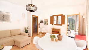 Ein Wohnzimmer mit einem beigen Sofa, einem weißen Esstisch mit Stühlen, einer Pendelleuchte und Blick durch eine Glastür.