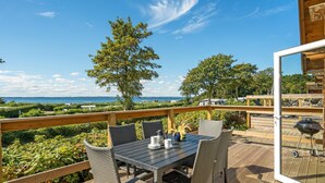 An outdoor deck with a table and chairs, overlooking a scenic view of the sea and greenery. - Cozy home in Tranekær (Tranekær)