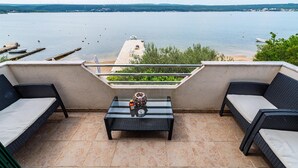 En terrasse med to fletsofaer, et glasbord og udsigt over en sø med både og vindmøller i horisonten.