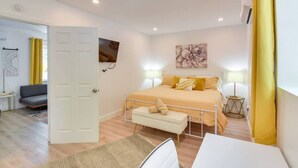 Un dormitorio con cama, mesitas de noche, una silla, un escritorio y un cuadro en la pared.