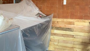 Una habitación con pared de ladrillo, suelo a cuadros y un objeto cubierto de plástico en el piso.