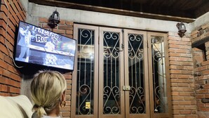 Una persona sentada en un sofá mirando la televisión en una habitación con paredes de ladrillo y techo de madera.