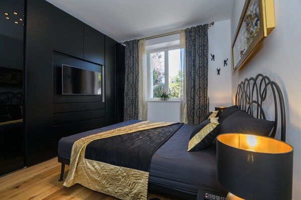 A modern bedroom with a large bed, a television mounted on the wall, and a window with curtains.