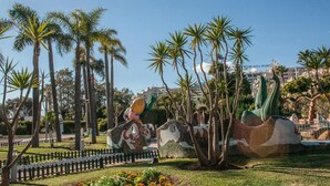 Un jardín ajardinado con palmeras, una escultura de mosaico y un edificio al fondo.