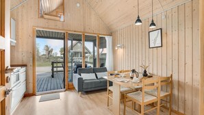 Ein gemütliches Blockhaus-Interieur mit Holzausstattung, einem Essbereich mit Tisch und Stühlen, einer Couch und Blick ins Freie.