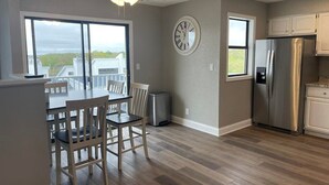 A modern kitchen with a dining area, large windows, and a clock on the wall.