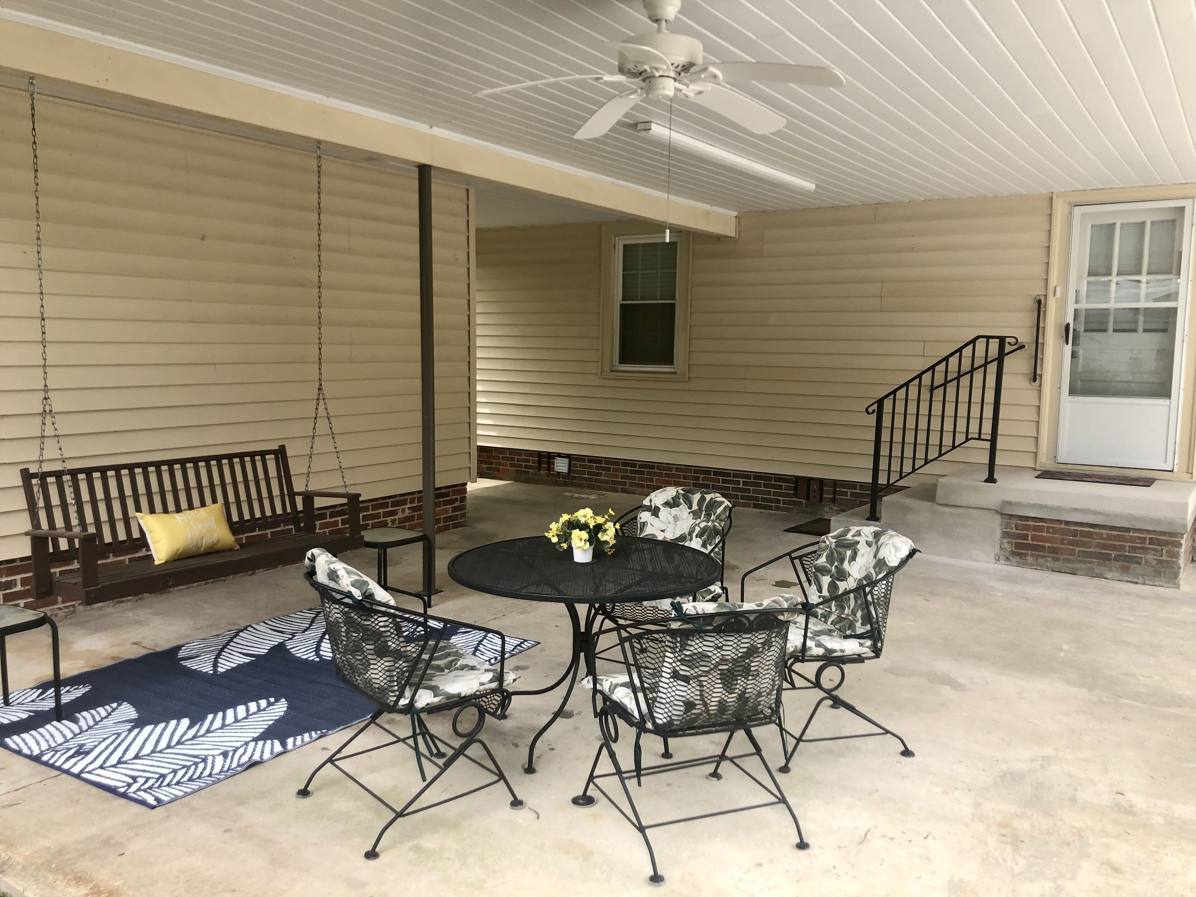 A covered patio with a swing, a round table with chairs, and a bench.