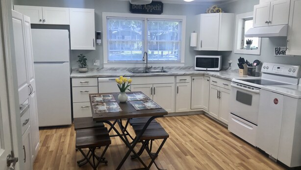 Una cocina con armarios blancos, una mesa de comedor de madera con bancos, un microondas, un horno y un ventilador de techo.