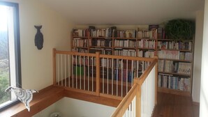 A room with a wooden staircase, a bookshelf filled with books, and a window with a view of trees.