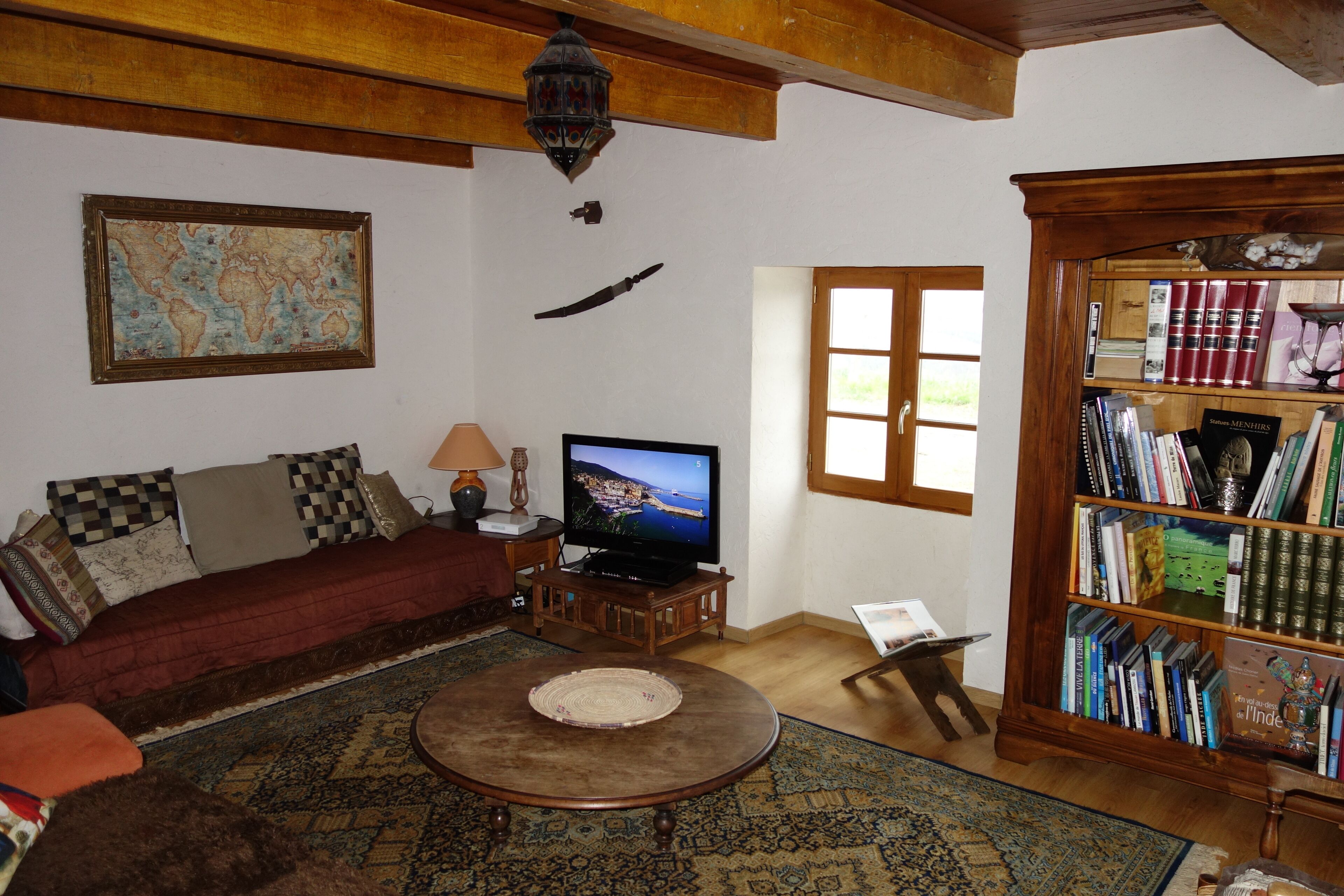 Una sala de estar acogedora con televisor, estantería, un mapa en la pared y ventana.