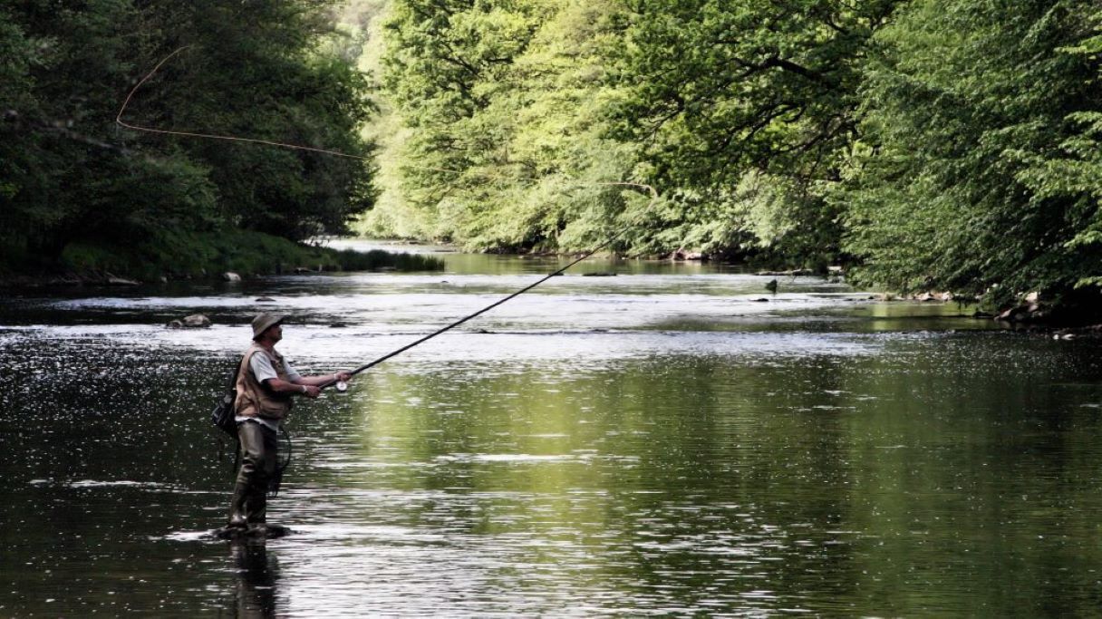 A person standing in a river, holding a fishing rod.