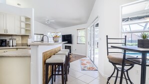 Uma cozinha moderna com ilha central, banquetas, mesa de jantar com cadeiras, televisão e lareira.