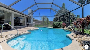 Piscina com área coberta, rodeada por um jardim paisagístico e um edifício com amplas janelas.