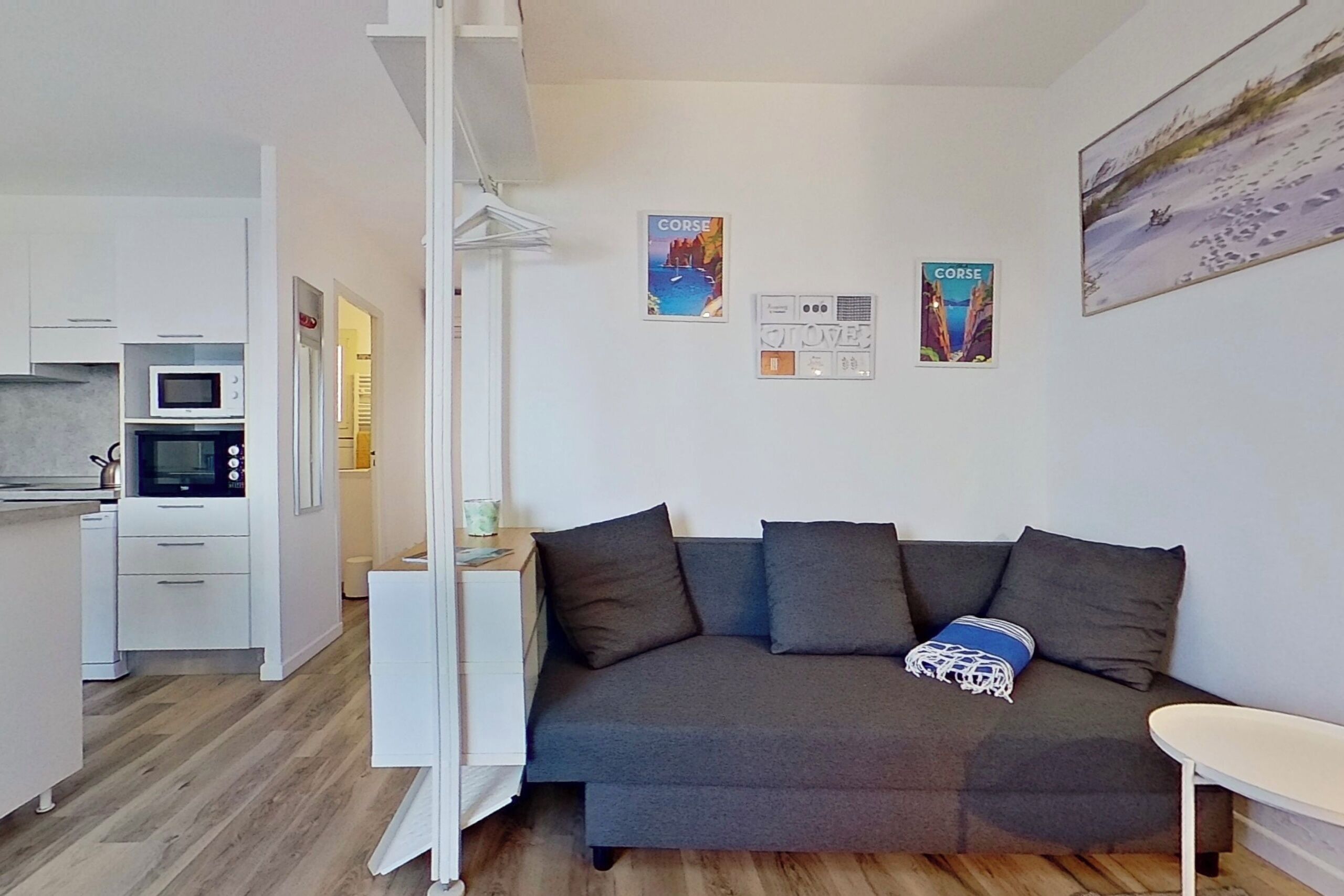 Un espacio habitable compacto con kitchenette, un sofá con cojines y dos carteles con motivos de viaje en la pared.