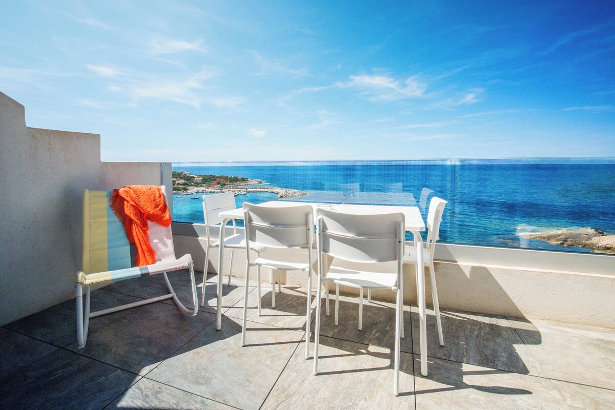 Une terrasse avec une table et des chaises, donnant sur une zone côtière aux eaux bleues et limpides.
