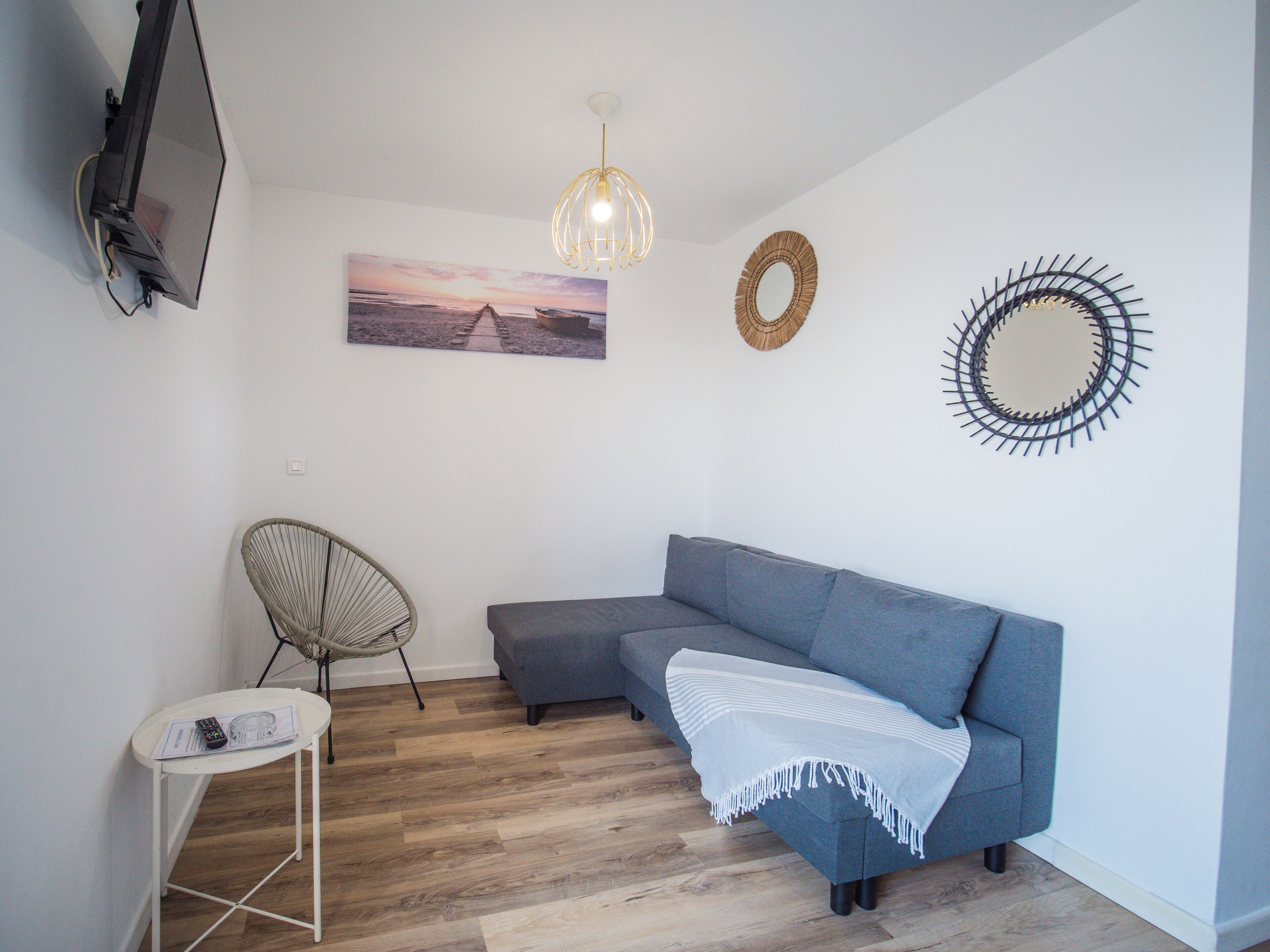 A modern living room with a grey sectional sofa, a white chair, a small white table, a TV mounted on the wall, and decorative wall art.